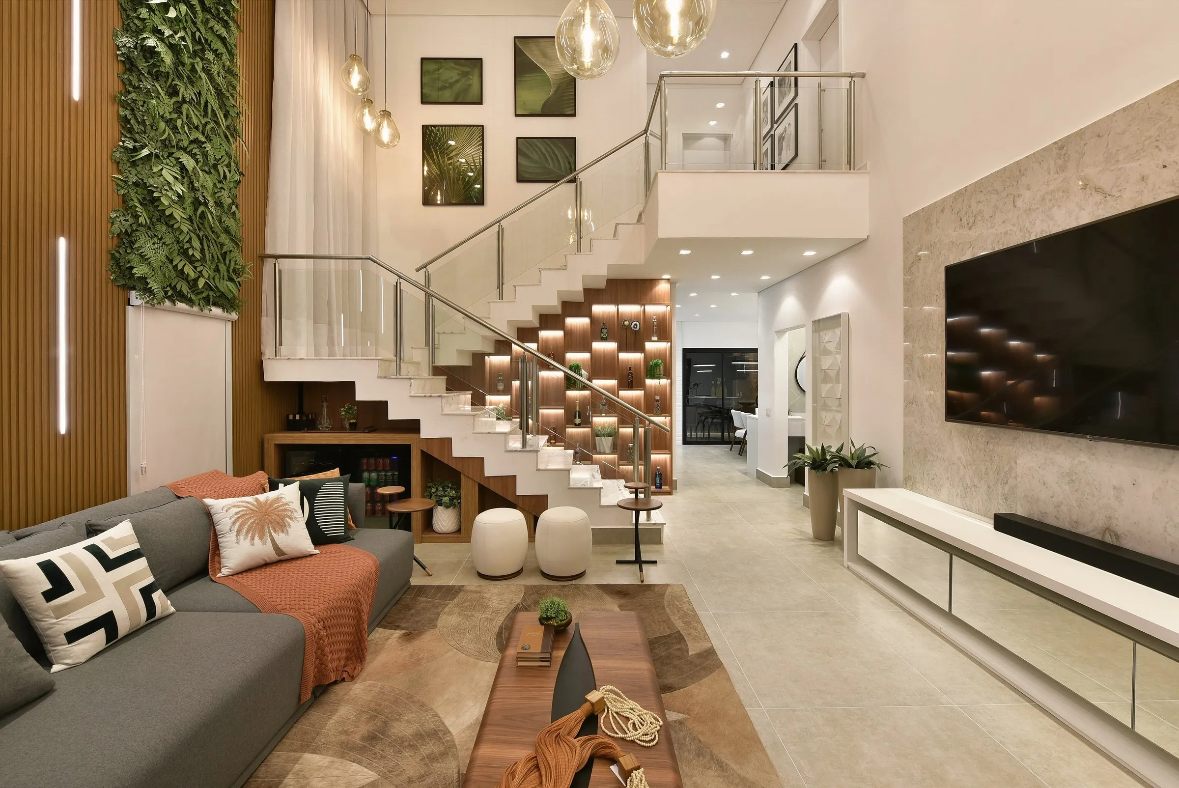 Sala com pé-direito duplo, escada com marcenaria iluminada e jardim vertical
